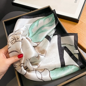 Elegant silk scarf featuring green floral prints and black borders on a luxury display