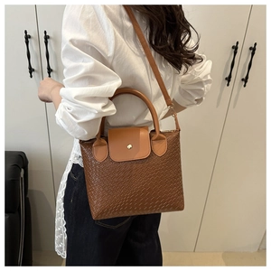 Lifestyle shot of a brown woven textured tote bag with top handle and gold metal clasp