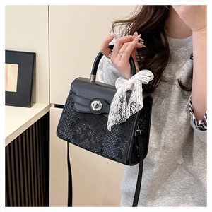 Detail of black snake-embossed crossbody bag with silver twist lock and lace bow charm