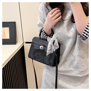Detail of black snakeskin texture handbag with silver lock and white lace bow detail