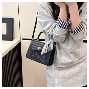 Detail of black Kelly bag featuring snakeskin texture and silver twist lock with lace charm