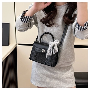 Detail of black snake-pattern leather bag with silver twist lock and lace bow charm