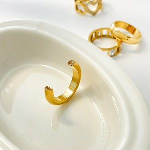 Detailed view of a gold open ring with zircons resting on a white ceramic bowl edge