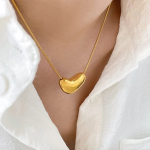 Gros plan du pendentif cœur doré sur une fine chaîne serpent portée par un mannequin