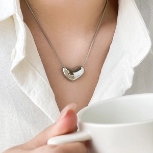 Détail macro du pendentif cœur poli et de la chaîne serpent sur un modèle en chemise blanche