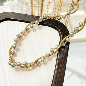 Detailed view of layered gold snake chain and silver bead chain on wood prop