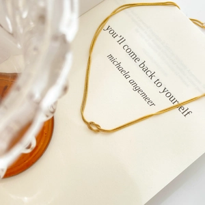 Detail of double-layer gold snake chain necklace featuring a minimalist polished knot pendant