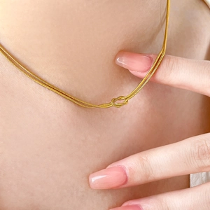 Detail of 18K gold-plated double-layer snake chain with central knot design worn by model