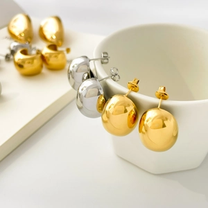 Polished gold and silver dome stud earrings and chunky C-hoops on a white ceramic cup