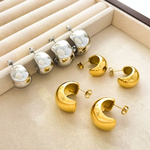 Close-up of polished 18K gold and silver dome hoop earrings on a velvet display tray