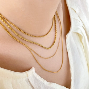 Detail of layered gold-plated titanium necklaces featuring snake and Cuban link chains
