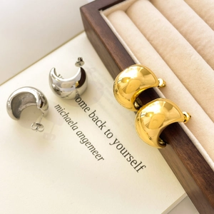 Polished gold and silver dome hoop earrings displayed on a rustic wood and beige background