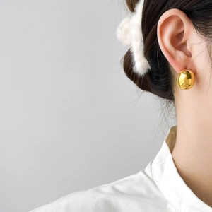 Close-up of model wearing polished gold teardrop stud earrings in minimalist style