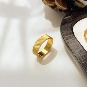 Détail macro d'une bague dorée en titane avec texture côtelée sur plateau en bois