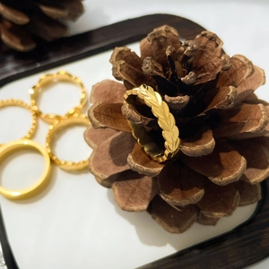 Détail d'un ensemble de bagues dorées avec motif feuille et anneaux fins sur une pomme de pin