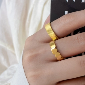 Détail d'une bague cœur dorée et d'un large anneau à rayures verticales superposés