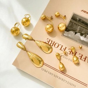 Golden titanium steel teardrop and spherical earrings displayed on a vintage magazine