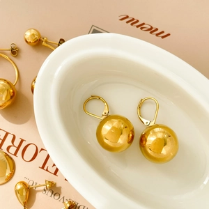 Detailed close-up of golden spherical earrings and studs arranged on a white ceramic tray