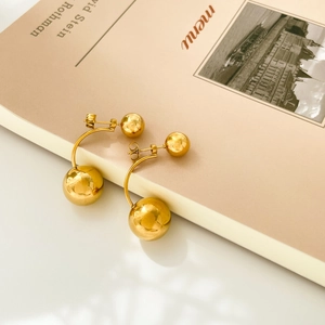 Macro shot of minimalist gold double ball curved earrings on a beige aesthetic background