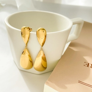 Macro shot of polished gold teardrop earrings hanging on a ceramic cup with smooth finish