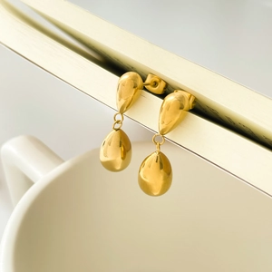 Close-up of golden teardrop earrings hanging on book pages with a polished mirror finish
