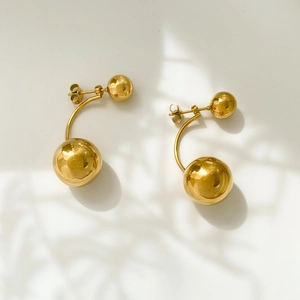 Detailed view of gold sphere earrings with polished metallic finish and curved link