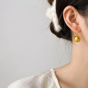 Macro shot of polished gold spherical earring with glossy mirror finish on a female model