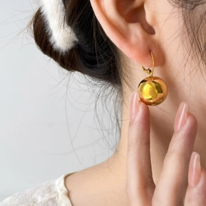 Minimalist golden polished sphere drop earrings worn by a model in a high-fashion pose