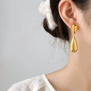 Elegant gold teardrop earrings in polished stainless steel worn by a model