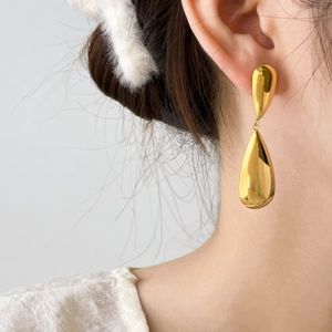 Macro detail of polished gold teardrop earrings showing elegant dangling metallic design