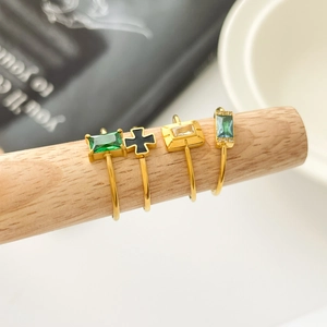 Detail of four 18K gold plated rings with emerald zircon and cross icons on wood props