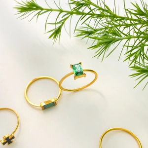 Detail of 18K gold plated rings set with green zircon stones and black cross charm