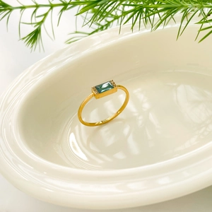 Close-up of gold titanium ring featuring a green emerald-cut zircon on white ceramic
