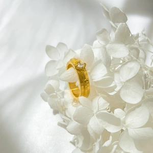 Close-up of golden square zircon ring with double-layered band among white flowers