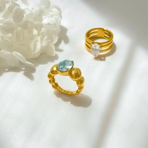Detail of gold rings with light blue oval gemstone and white teardrop stone on white fabric