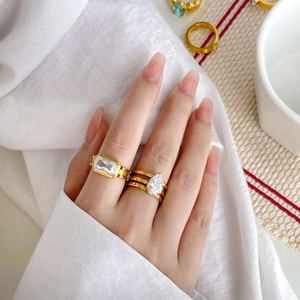 Detail of gold-plated rings with pear and emerald cut zircons on soft white fabric