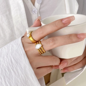 Close-up of gold layered rings with pear-cut zircon on model holding a white cup