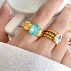 Gold rings with blue oval zircon and pear-shaped white stone on woman's hand