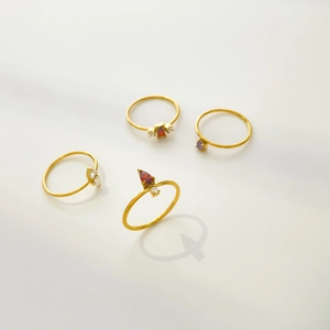 Close-up of four stackable 18K gold plated rings with red and purple gemstones