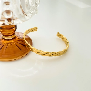 Detail of twisted gold-finish woven cuff bracelet with triple-layered arched metal design