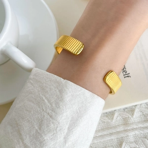 Close-up of golden grooved wide cuff bracelet worn by a model in elegant urban style