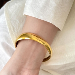 Close-up of a wide polished gold cuff bracelet with a smooth curved surface on a wrist