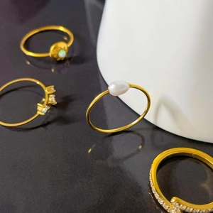 Dettaglio di un set di quattro anelli d'oro in titanio con perle, zirconi e opali