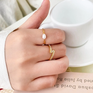 Dettaglio di un anello a fulmine dorato e un elegante anello con perla vicino al caffè