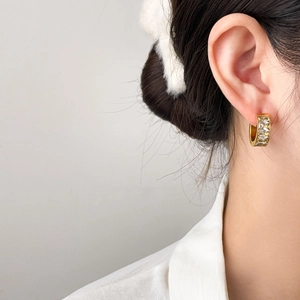 Gros plan d'une boucle d'oreille dorée avec zircons carrés sur l'oreille