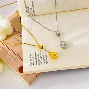 Minimalist gold and silver water drop necklaces on a book with soft lighting