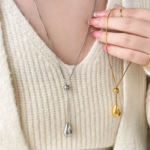 Gold and silver teardrop pendants on snake chains over a beige knit sweater