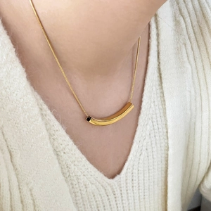Close-up of minimalist 18K gold-plated curved tube pendant on a fine snake chain