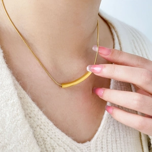 Detailed view of an 18K gold plated curved tube pendant necklace on a knit sweater