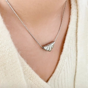 Close-up of a silver croissant pendant necklace with pleated texture on white knitwear